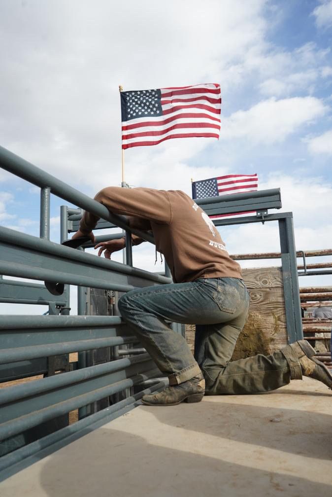 A man climbing the chutes with American flags flying above the arena gate