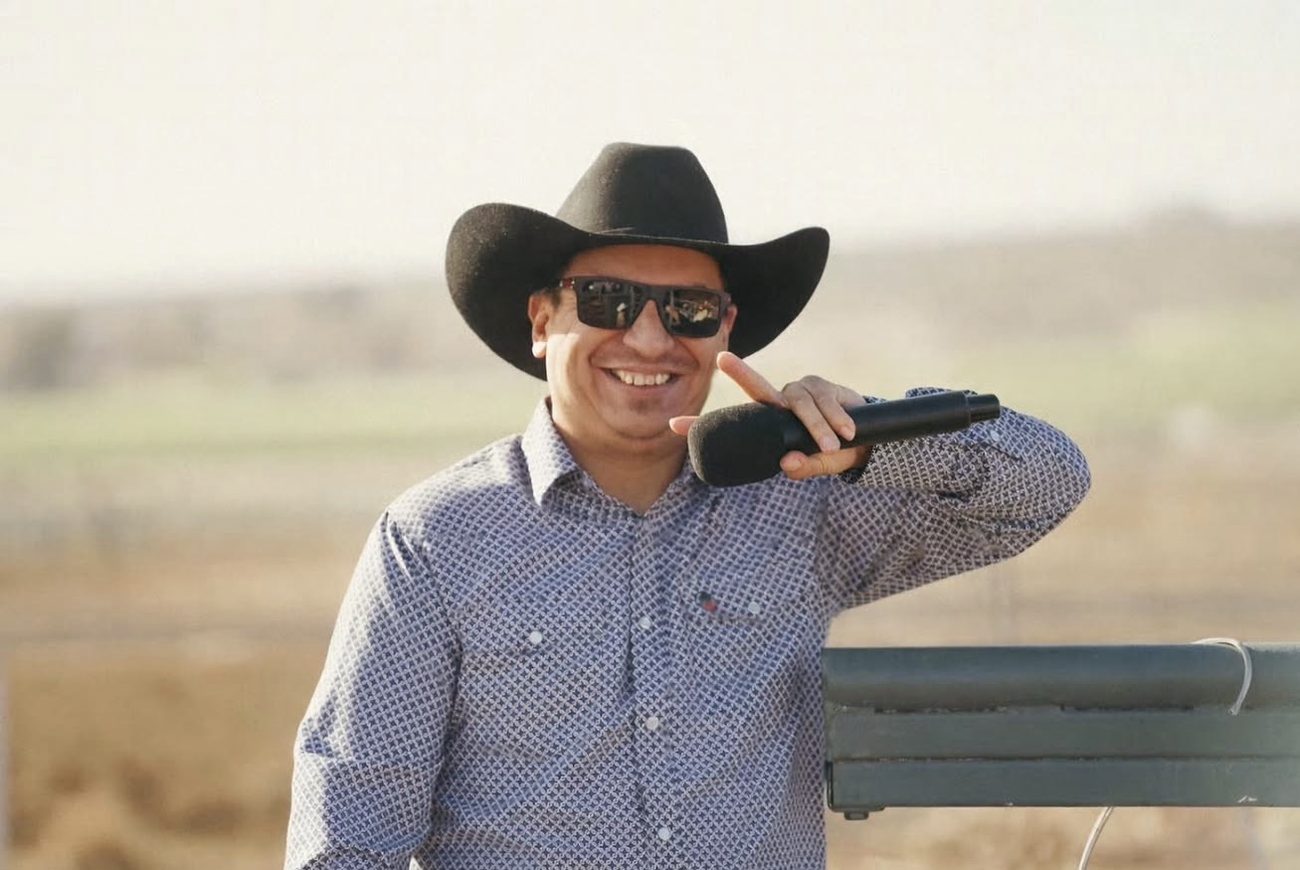 Pastor Charlie Salazar in a black cowboy hat, smiling with a microphone in hand at an outdoor gathering