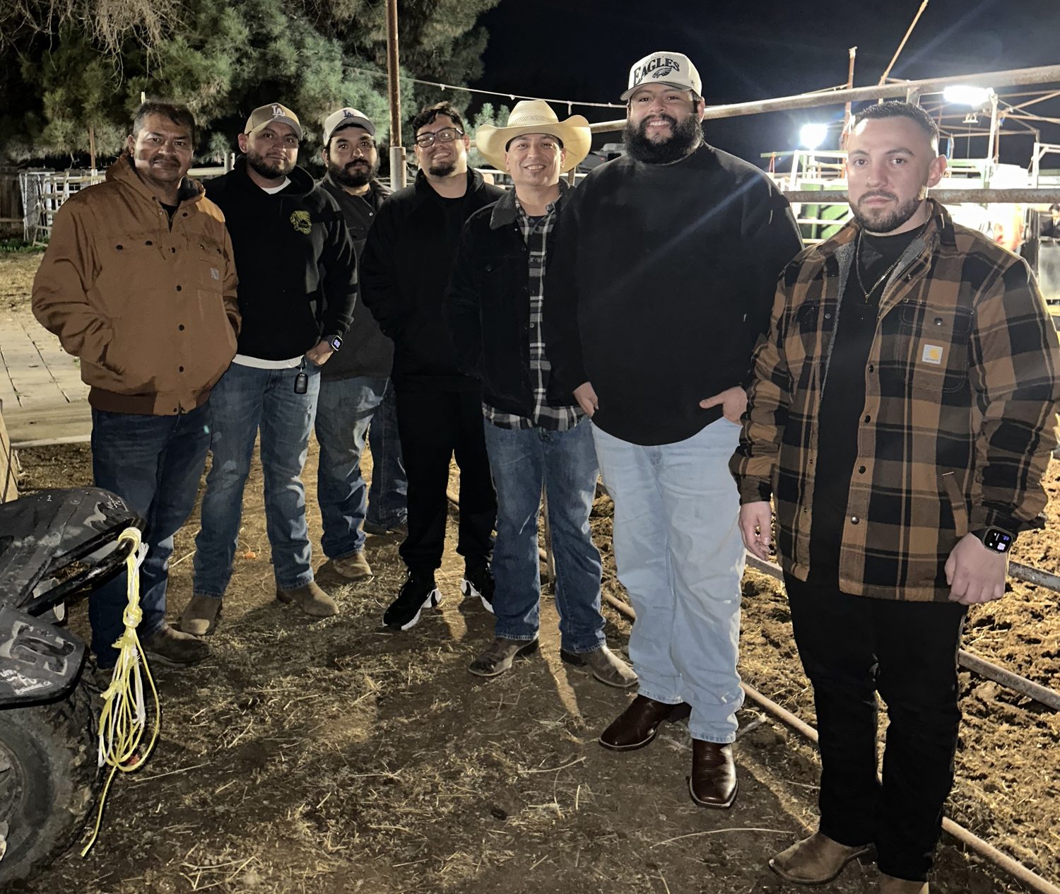 Seven men standing together under a work light at the arena after dark
